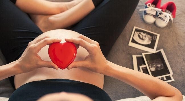 A pregnant woman holding a heart above her pregnant belly