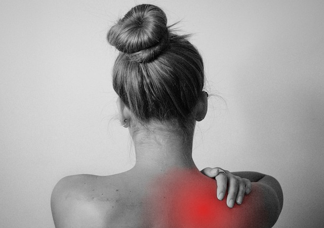 A woman holding the back of her right shoulder